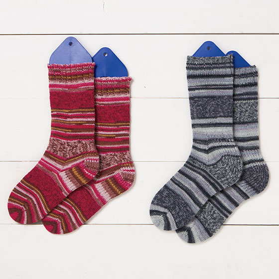 Two at Once, Toe Up, Magic Loop Socks pattern. On a white board background, Two sets of socks on sock blockers, knitted using Static Self-Patterning Sock Yarn by Knit Picks.