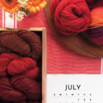 A July 2021 calendar with an image of a pile of red yarn, a box of red yarn, and some yellow flowers